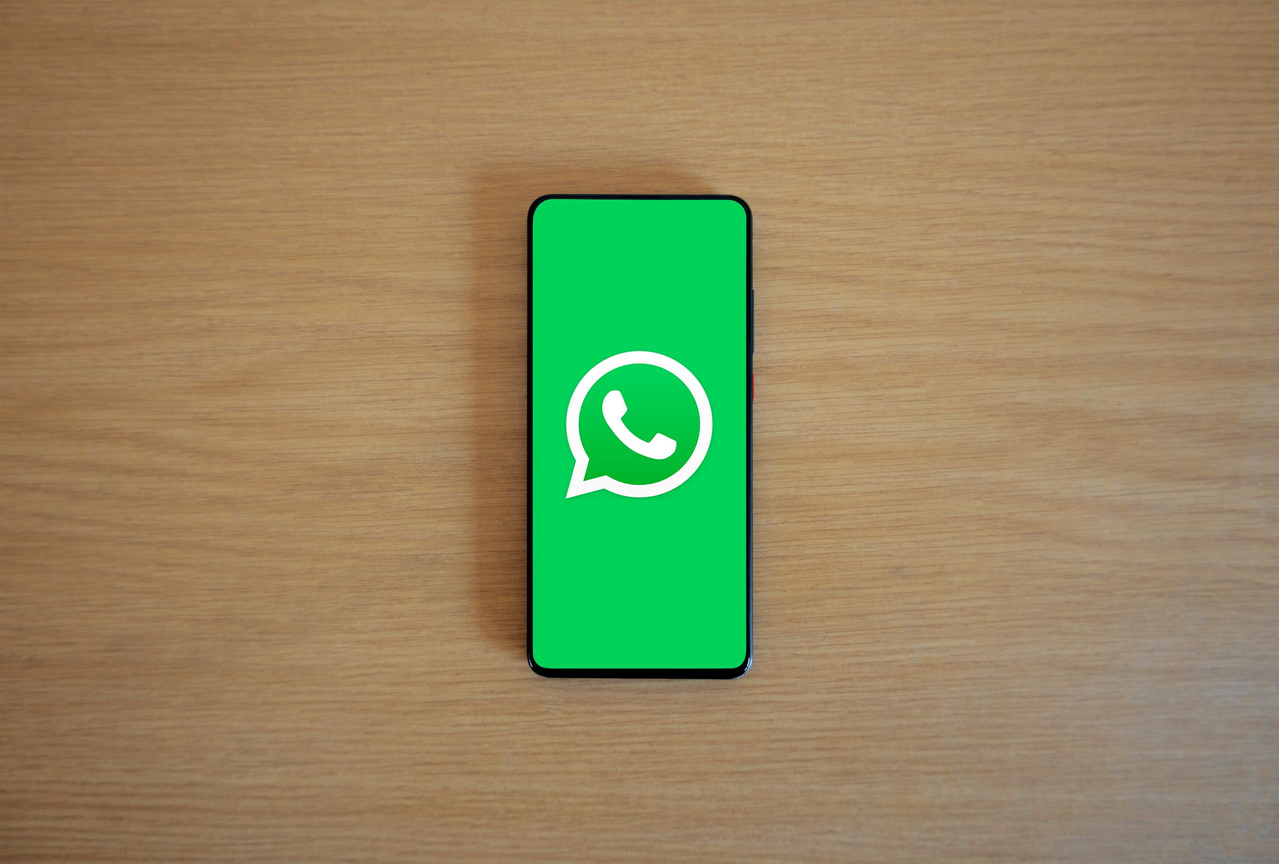 Top view of smartphone displaying WhatsApp logo on a wooden background, representing technology and communication.